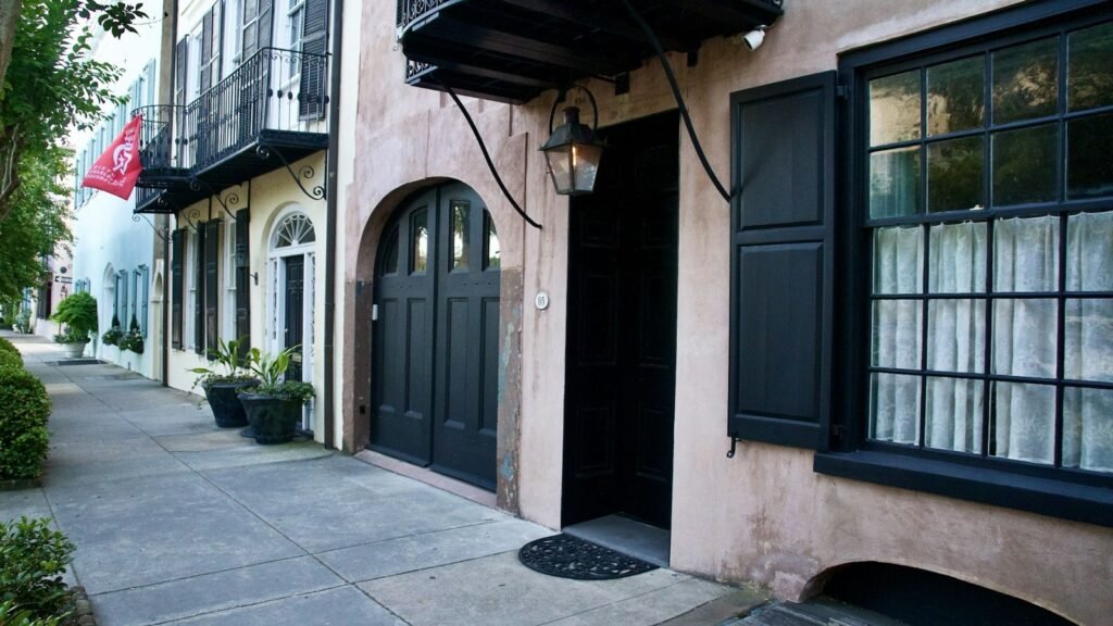 Gas lantern and black-shuttered doors on a pastel row of historic houses on a quiet Charleston sidewalk