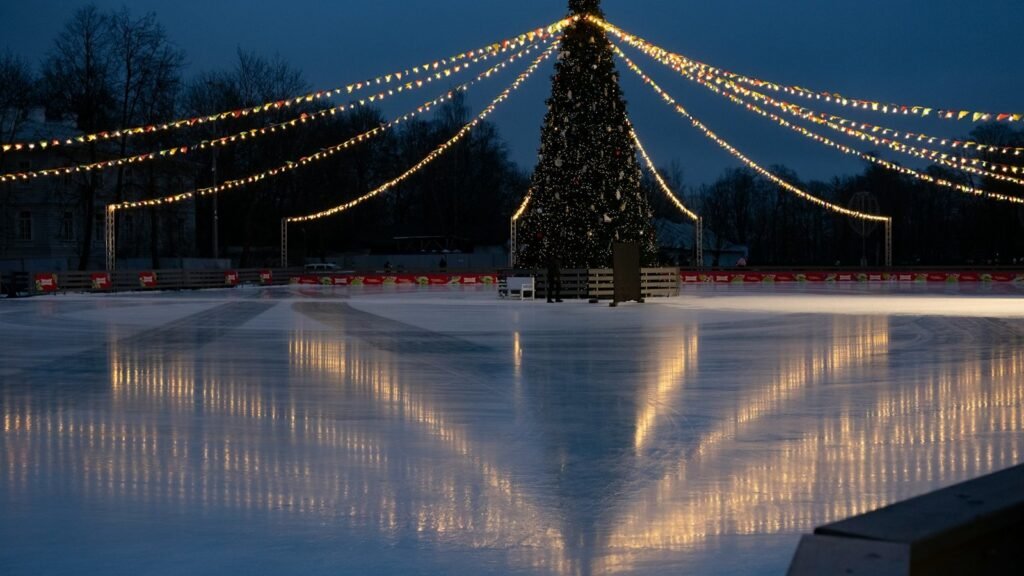 A lit Christmas tree with strings of lights over an outdoor ice rink at dusk