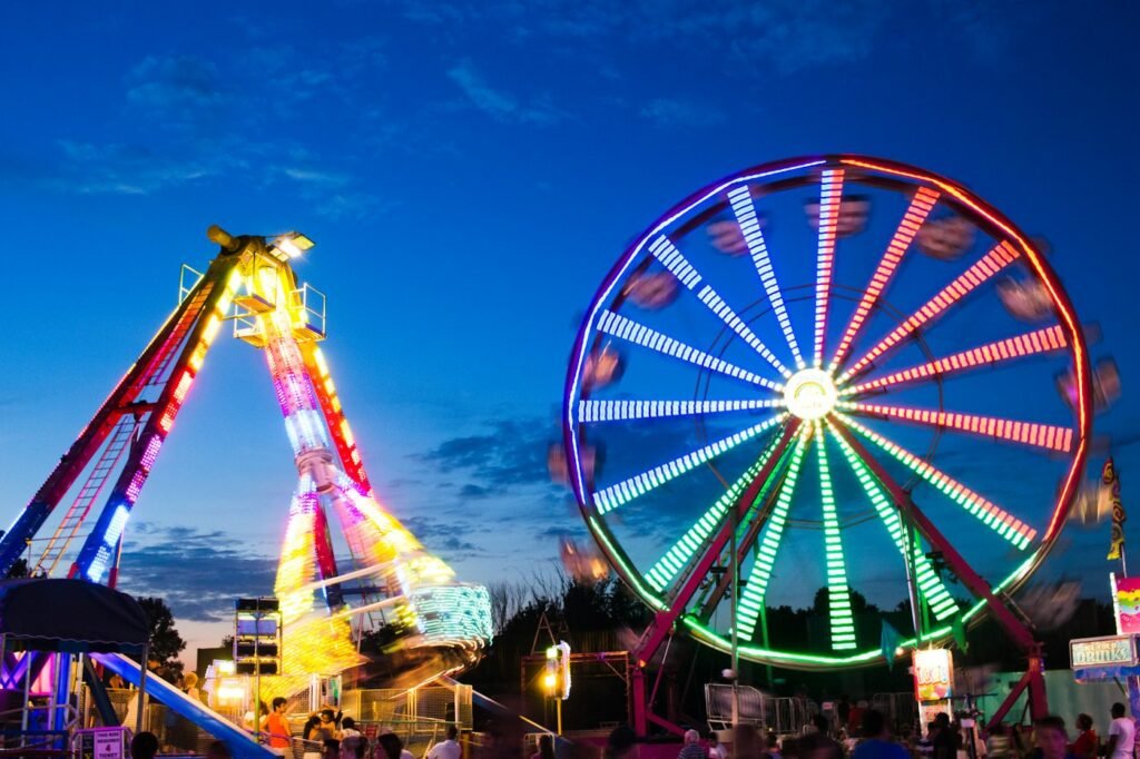 A lit-up ferris wheel and swinging ride glowing against a deep blue dusk sky at a county fair