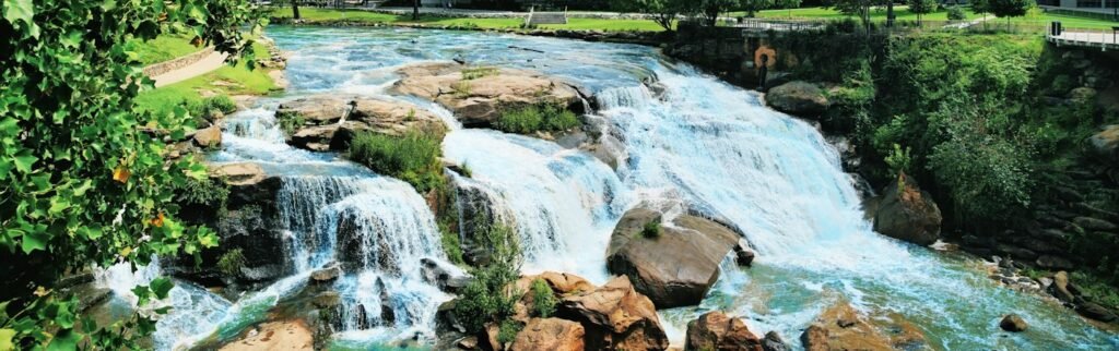 The Reedy River Falls tumbling over rocks beside green trees at Falls Park on the Reedy in downtown Greenville