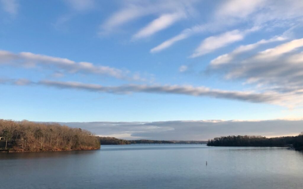 Wide calm lake with wooded points under streaky clouds and blue sky