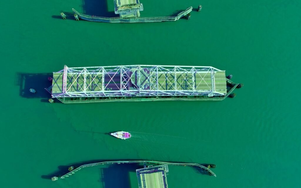 Overhead view of a green steel swing bridge turned open over green water with a small boat passing