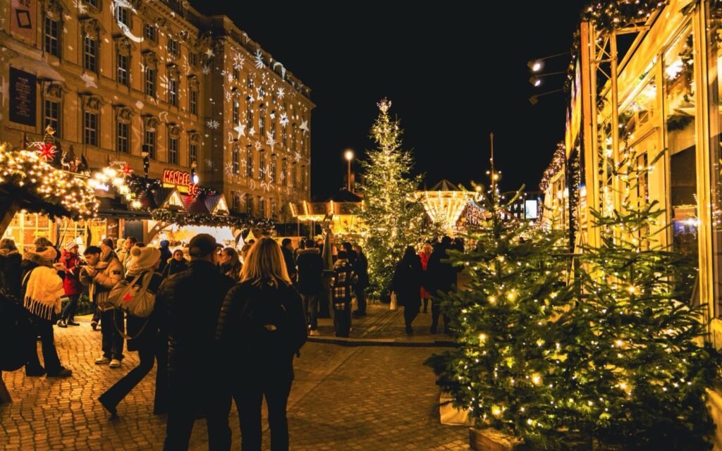 Night Christmas market with lit stalls, decorated trees and shoppers walking between them