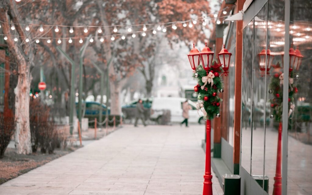 Downtown sidewalk strung with warm lights, red lantern posts with wreaths and bare winter trees