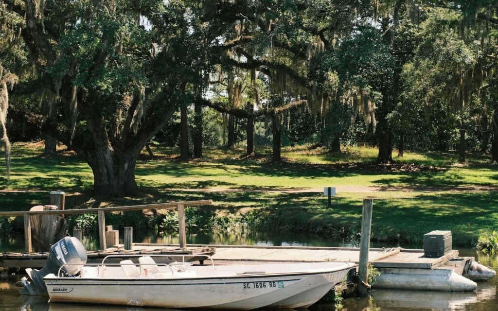 White motorboat tied to a small wooden dock on calm water under moss-draped live oaks