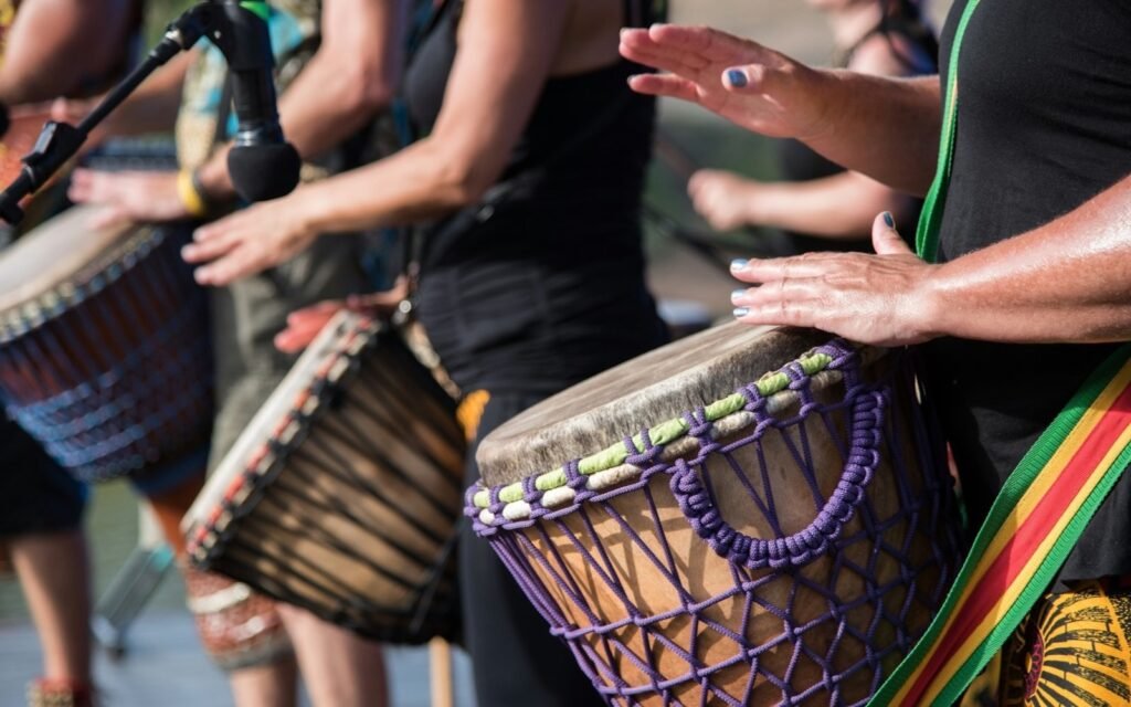 Hands of drummers playing djembe drums at an outdoor celebration, faces out of frame