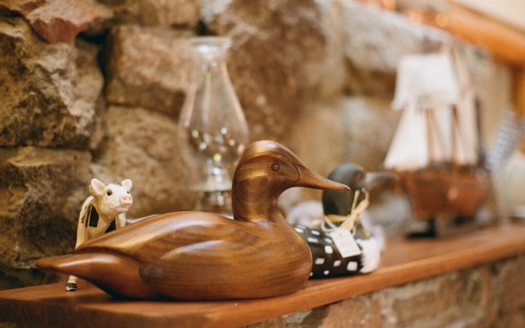 Carved wooden duck decoy resting on a rustic shelf in front of a stone wall