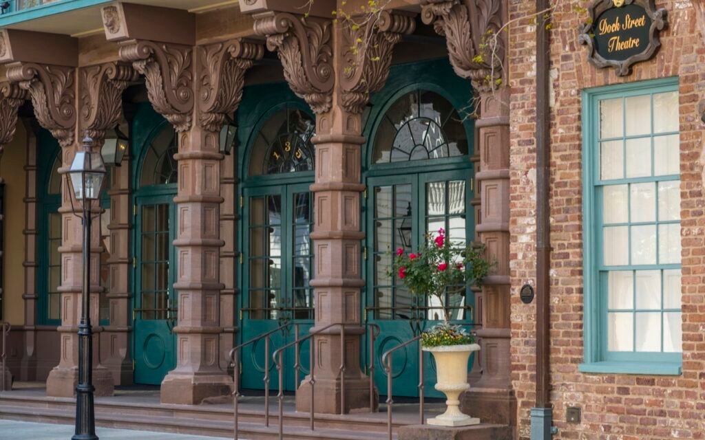 Arched brownstone entrance and teal doors of the Dock Street Theatre on a brick street in Charleston