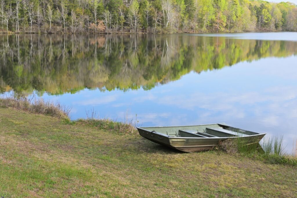 Calm lake reflecting a tree line on a spring morning with a small boat on the grass bank