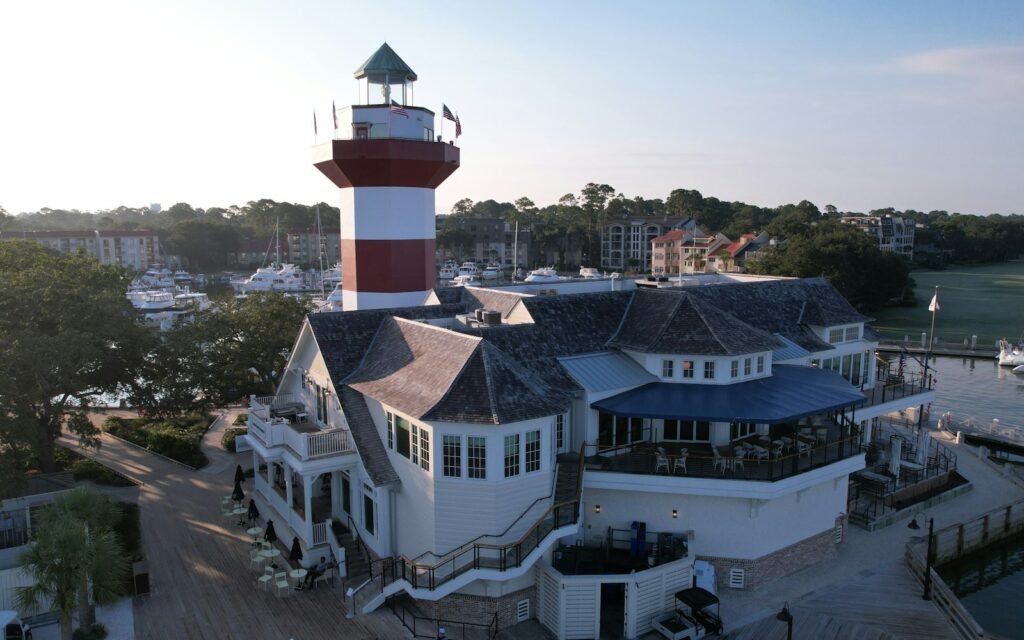 Red-and-white Harbour Town lighthouse rising over a white harborside building and marina on Hilton Head