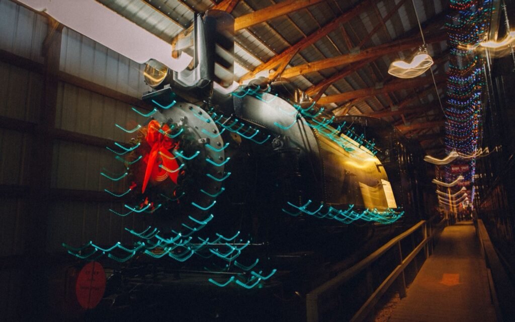 Vintage black steam locomotive inside a train shed, outlined with streaks of colorful Christmas lights