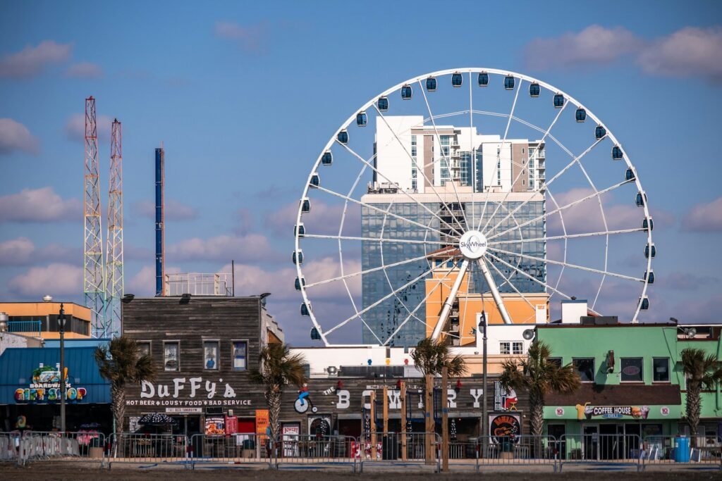 Myrtle Beach SkyWheel ferris wheel rising behind boardwalk shops and palm trees