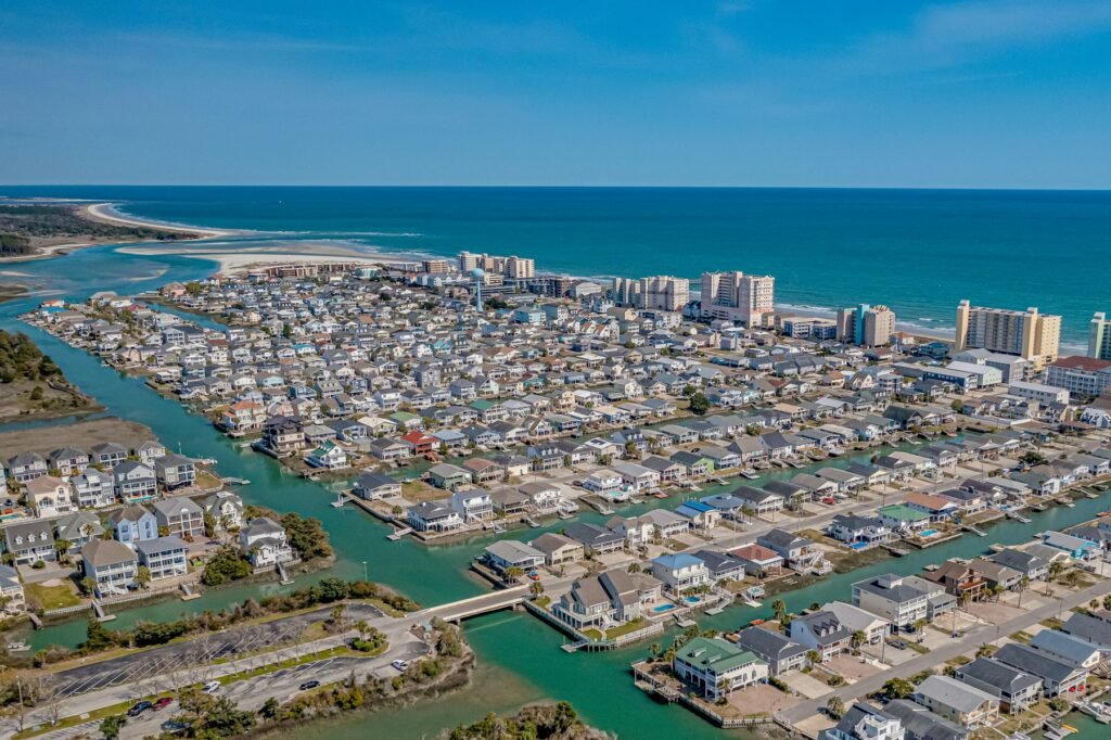 Aerial view of dense beach houses along canals beside the ocean and a pier in the distance