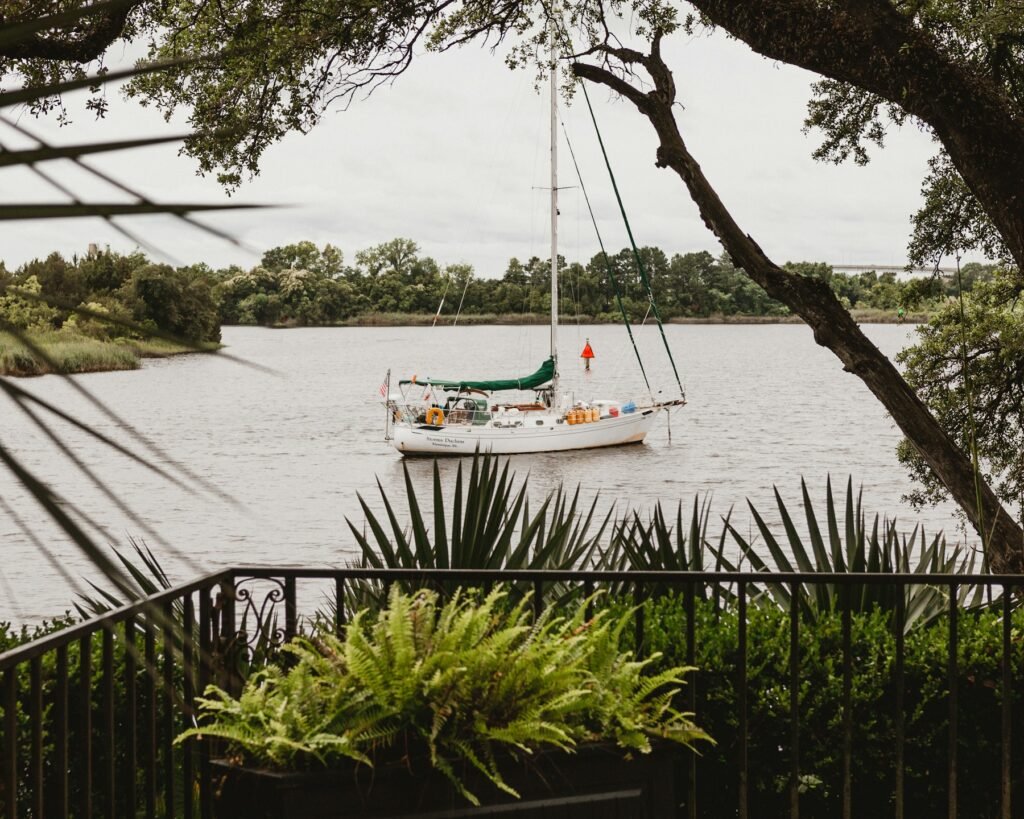 Sailboat moored on a calm river viewed through tropical foliage and palms from an iron railing