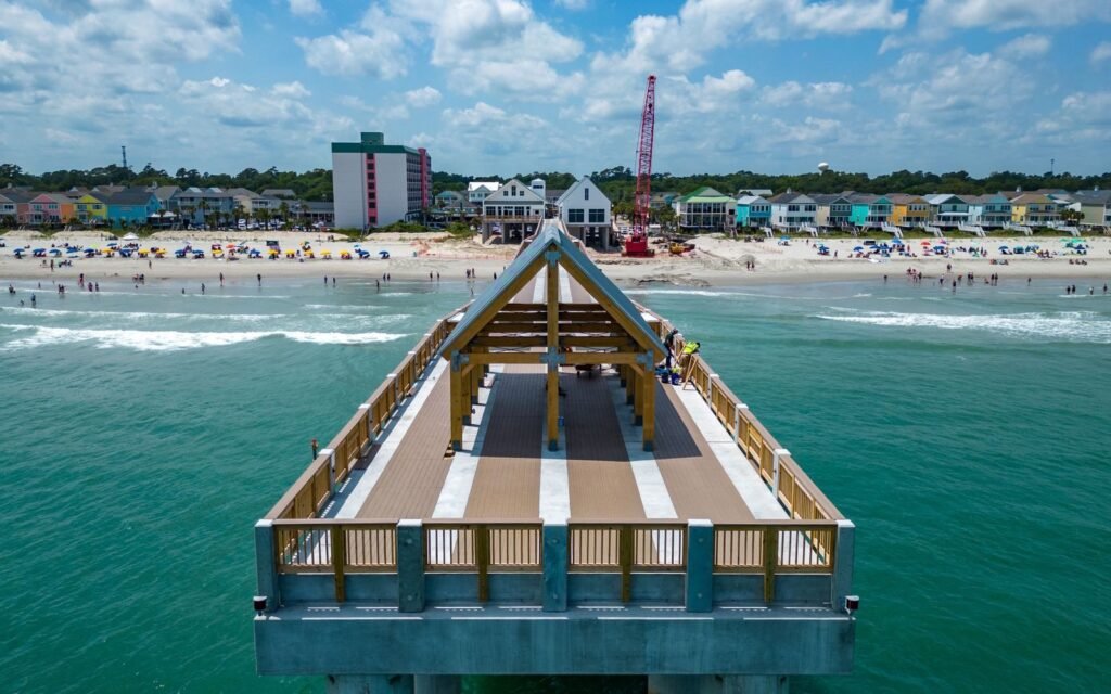 Aerial view of the Surfside Beach pier end over green surf with the beach and colorful houses behind