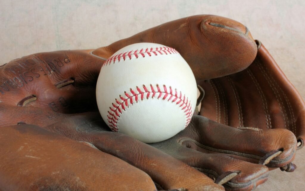 White baseball with red stitching resting in a worn brown leather glove
