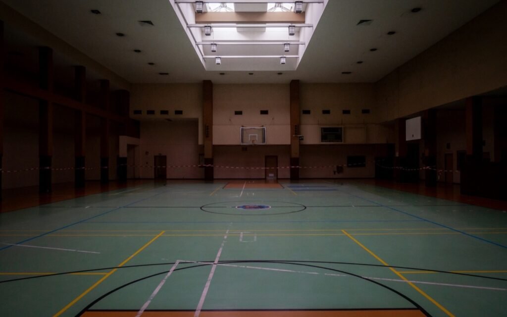 Empty indoor basketball court with painted lines and hoops under dim lights