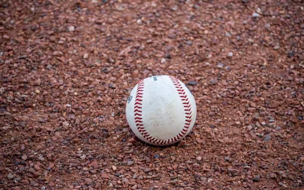 Single scuffed baseball sitting on reddish infield dirt