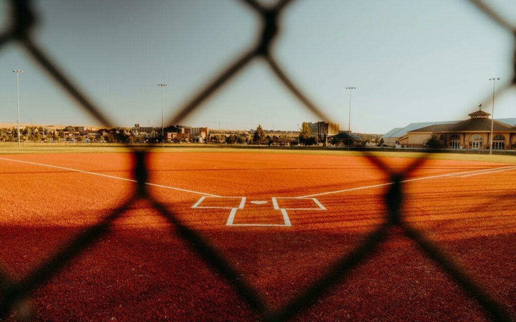 Baseball diamond home plate seen through a chain-link fence in late golden light
