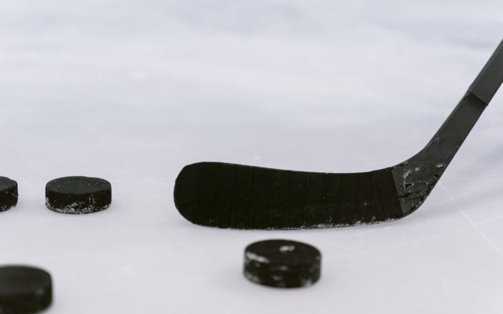 Black hockey stick blade and several pucks resting on scratched white ice
