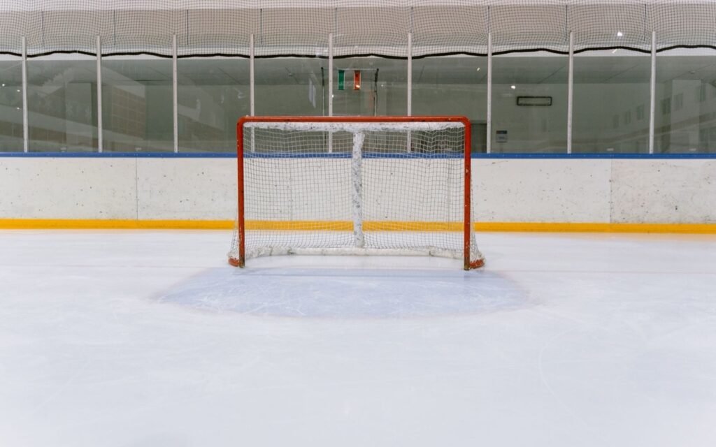 Empty ice hockey rink with a red goal net in front of the boards and glass