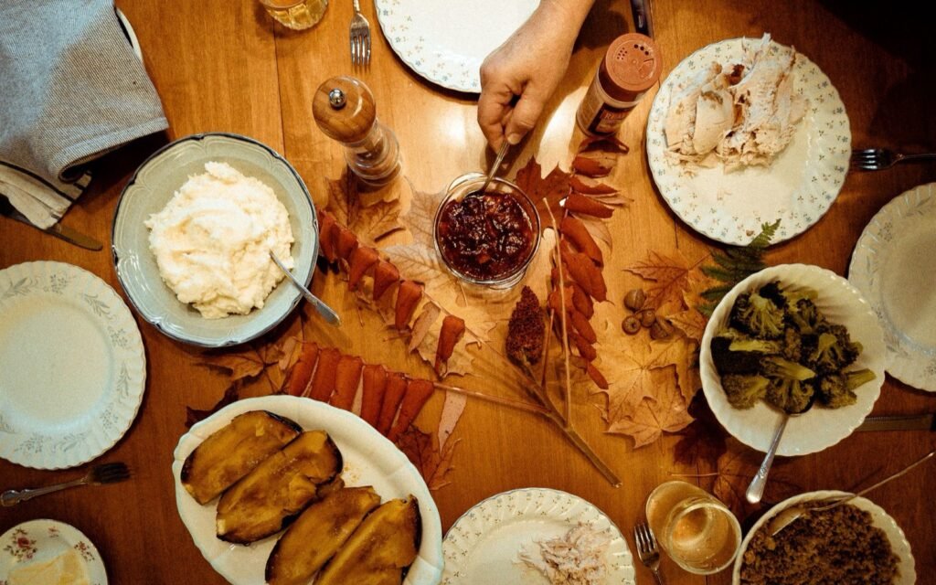 Overhead view of a Thanksgiving table with turkey, sweet potatoes, mashed potatoes, cranberry sauce and fall leaves