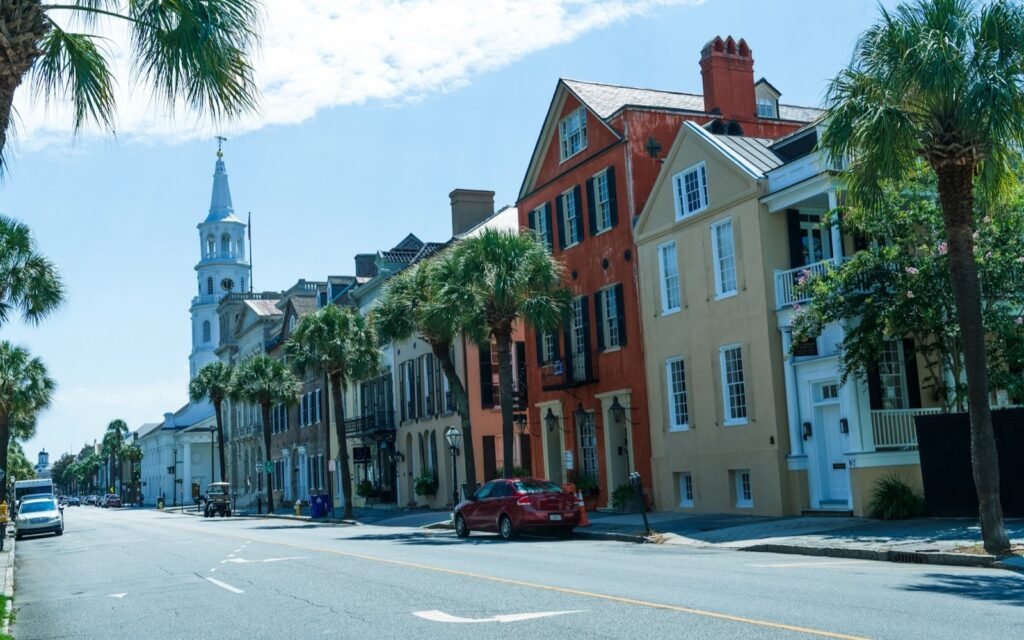Sunny Charleston street lined with palmettos, brick and pastel historic houses, and a white church steeple