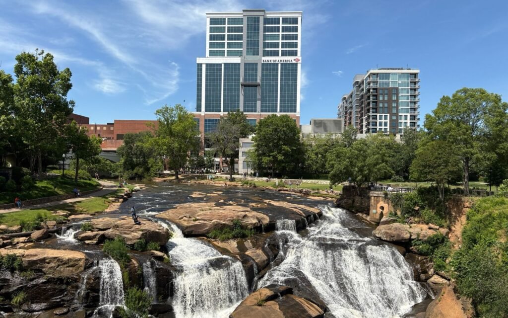 Reedy River Falls tumbling over rocks in Falls Park with downtown Greenville towers behind