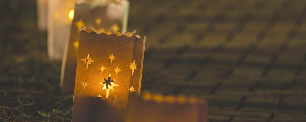 Paper luminaria bag with star cutouts glowing with a candle along a path at night