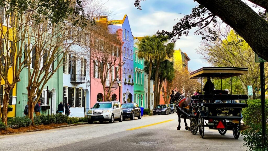Pastel row houses and palmetto trees on a Charleston street with a horse-drawn carriage on the right