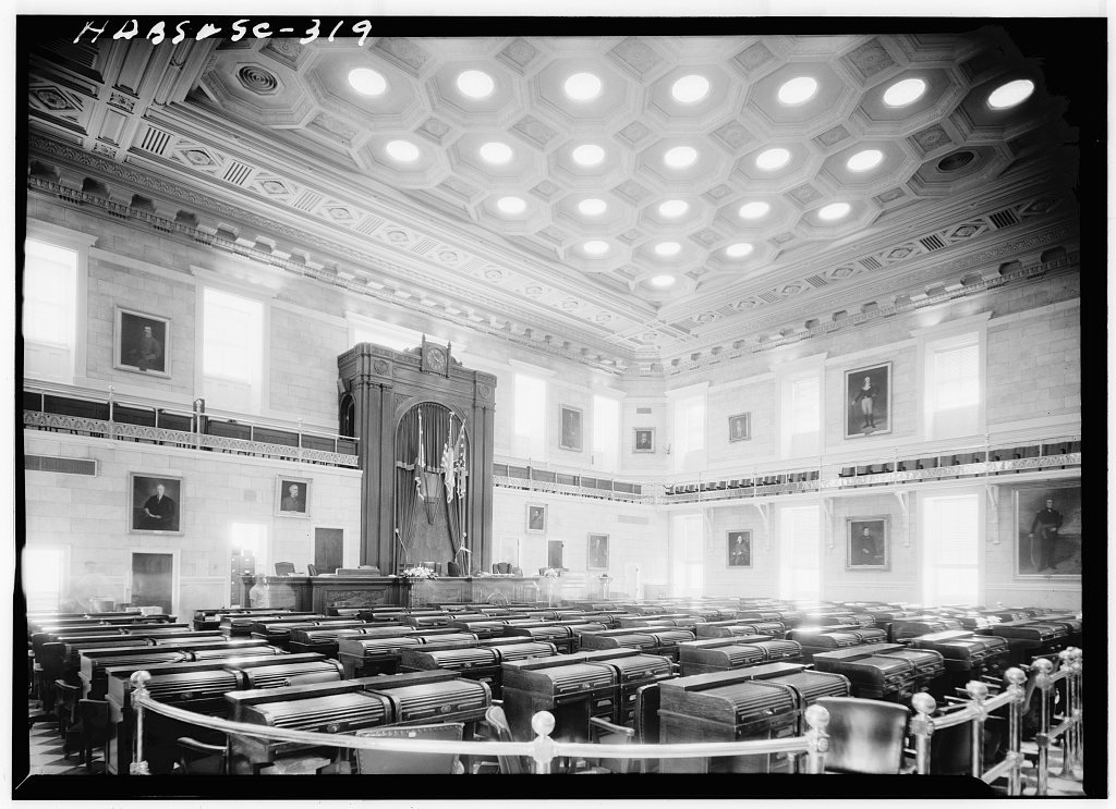 Rows of wooden desks in a legislative chamber of the South Carolina State House, under a coffered ceiling