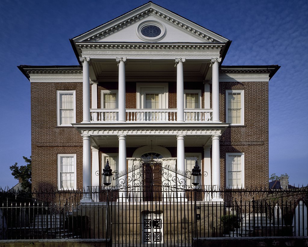 Two-story brick Miles Brewton House with a columned portico behind an iron fence in Charleston