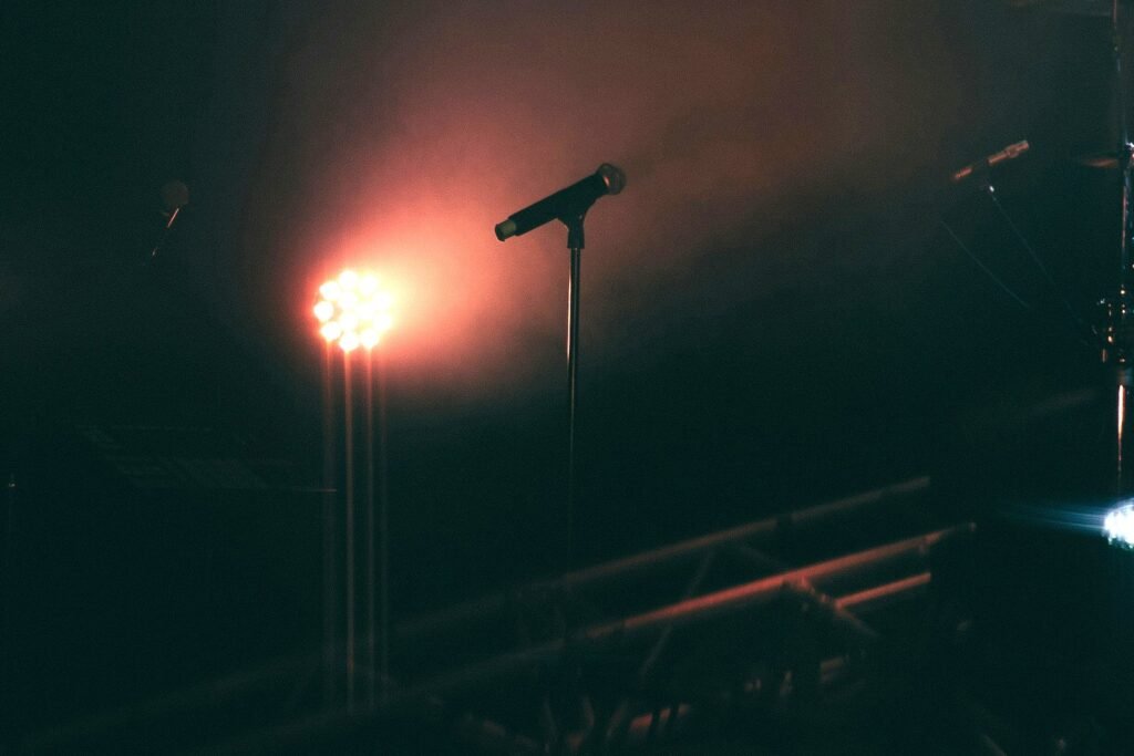 An empty concert stage in haze with a microphone on a stand beside a glowing red stage light